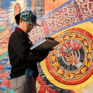 Woman with clipboard examining a mural.